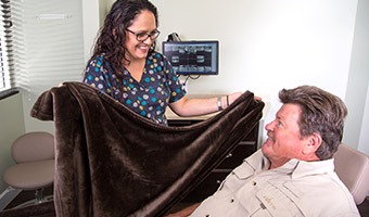 A dental assistant offering a fuzzy blanket to a patient in a dental exam chair. 