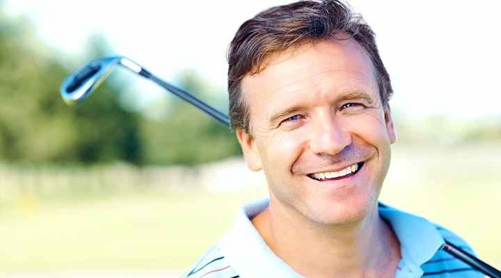 Smiling man with a golf club showing off his new teeth. 